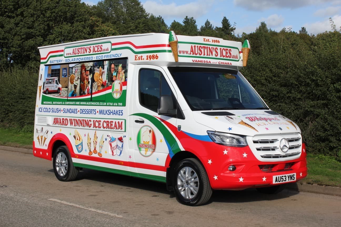 Austins Ices electric ice cream van seen from the front, with the roof sign reading Battery, Solar Powered, Eco Friendly and a menu board reading Award Winning Ice Cream
