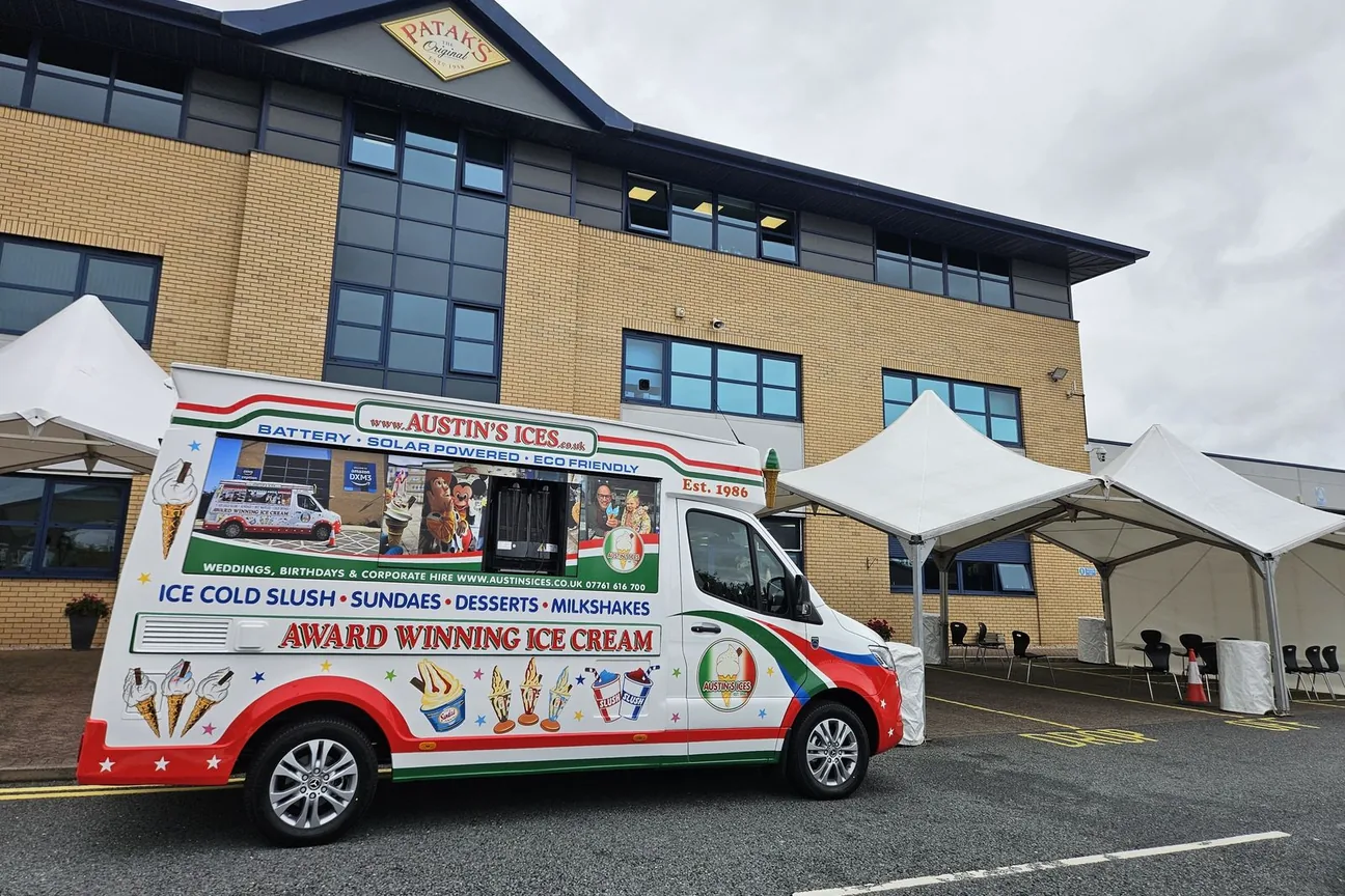 Austins Ices electric ice cream van set up beside white event gazebos outside a corporate building